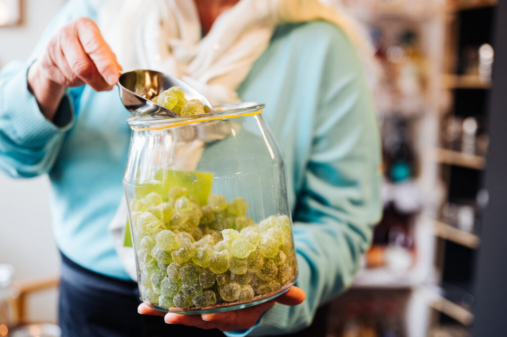 Eine Person hält ein Glas mit grünem Fruchtgummi und löffelt einige aus dem Glas.