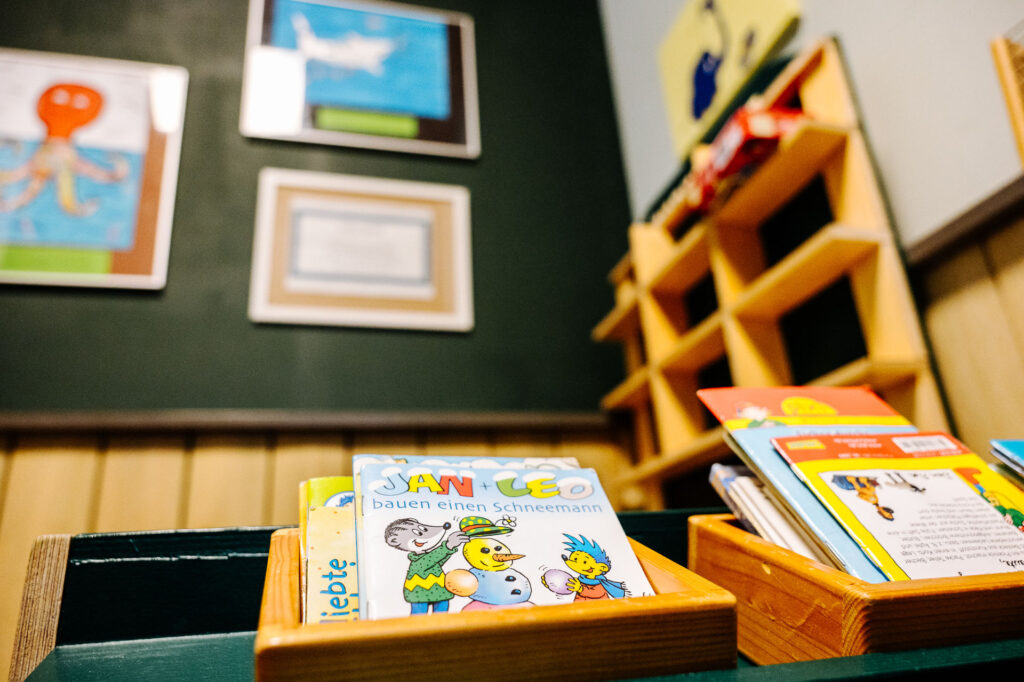 Kleine Geschichtshefte für Kinder in Behältern, die auf einem Regal in einer Kinderspielecke liegen.