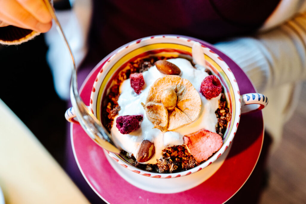 Eine Person hält einen Teller mit einer Müslischüssel, in dem sich Müsli, Joghurt und Trockenfrüchte befinden.
